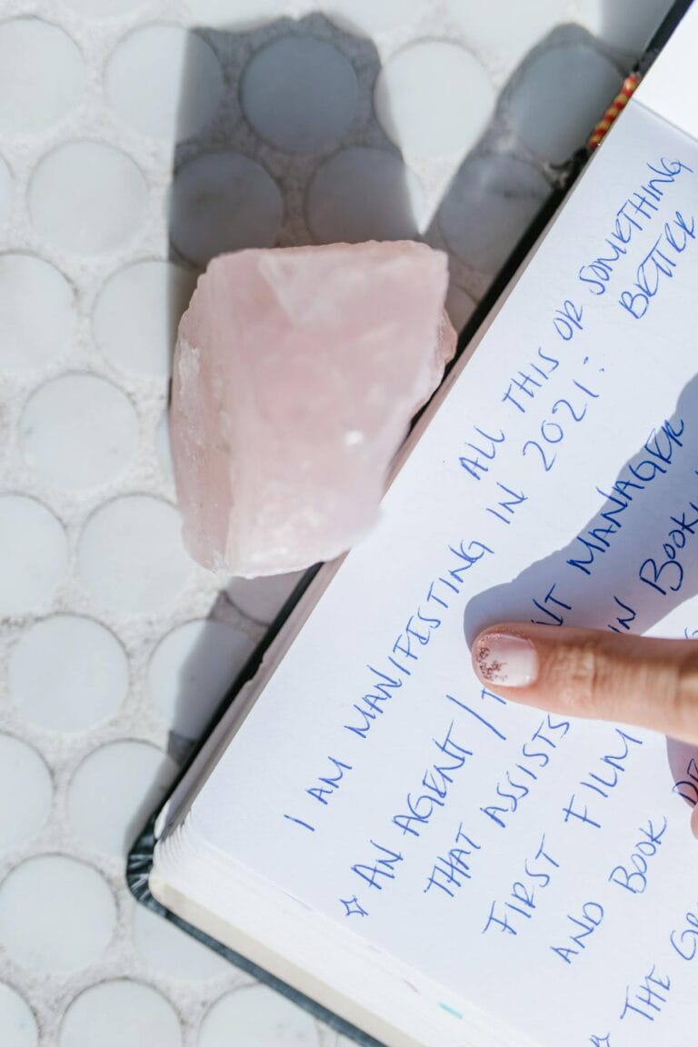Close-up of a manifestation journal page with a rose quartz crystal and finger pointing.